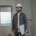 Adult male construction worker holding blueprints in an indoor renovation site.